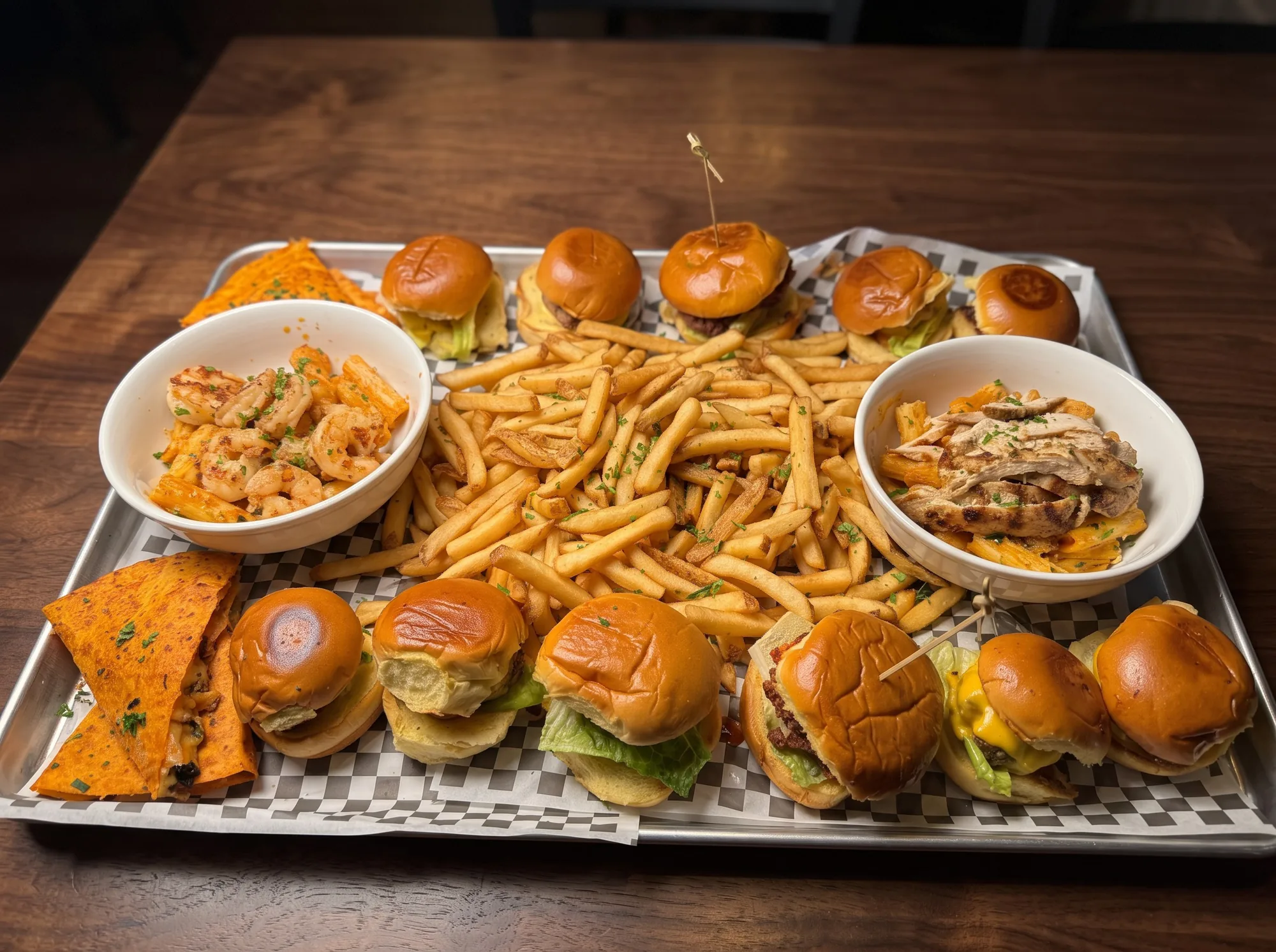 A Rush Hour party tray: sliders, fries, quesadilla and two bowls of pasta, on checkered paper
